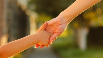 a parent holds the hand of a small child