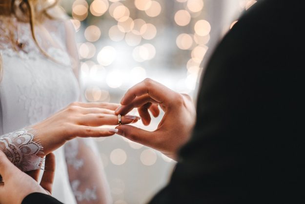 man placing wedding ring on woman's hand