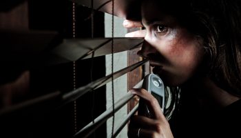Fearful battered woman peeking through the blinds to see if her husband is home