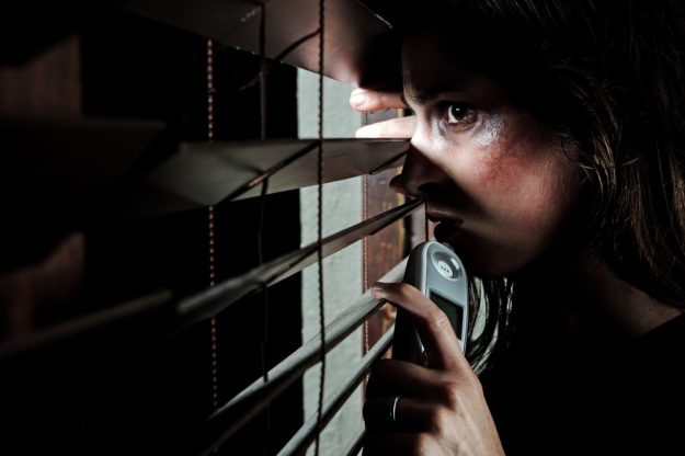 Fearful battered woman peeking through the blinds to see if her husband is home