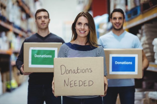 Volunteers smiling at camera holding donations boxes in a large warehouse