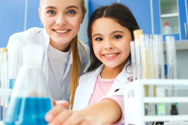 Teacher with little child in school laboratory bulb with liquid