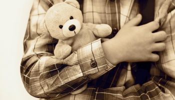 sepia image of little boy holding a teddy bear