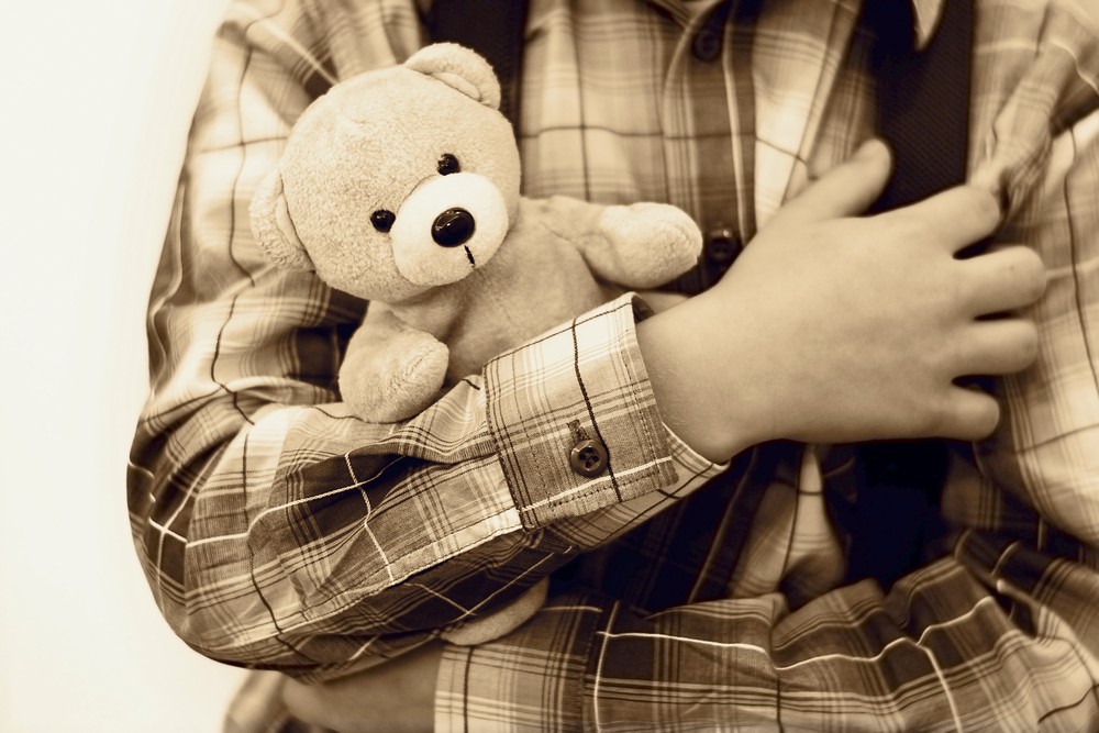 sepia image of little boy holding a teddy bear