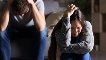 Sad couple after argument or breakup sitting on a sofa in the living room in a house