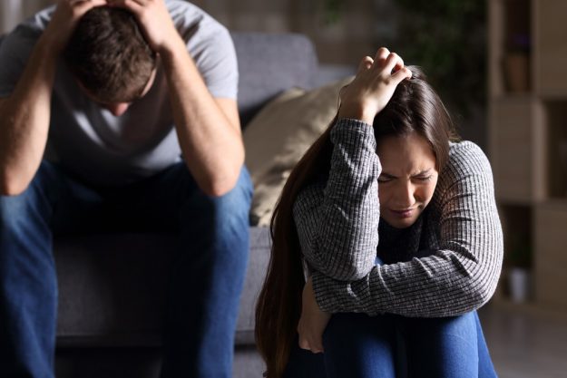 Sad couple after argument or breakup sitting on a sofa in the living room in a house