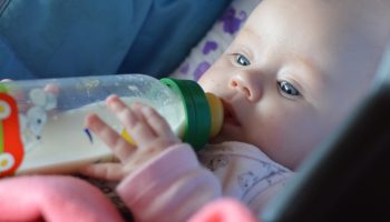 infant enthusiastically sucks a bottle of milk in a stroller for a walk