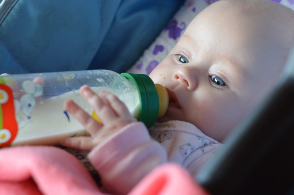 infant enthusiastically sucks a bottle of milk in a stroller for a walk