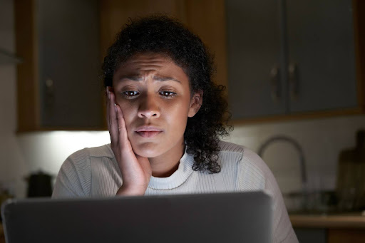 Concerned woman with curly hair resting her face on one hand, looking at a laptop screen in a dimly lit kitchen. what can be used against you in a custody battle 